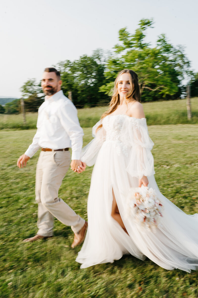 candid wedding picture with bride and groom holding hands and walking down a hill together while laughing at their charlottesville wedding
