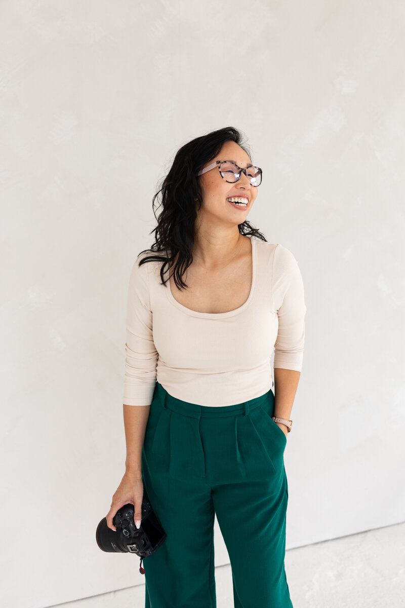 Anh Nguyen, photographer behind Anh Point Photography, smiling with a camera looking in the distance.