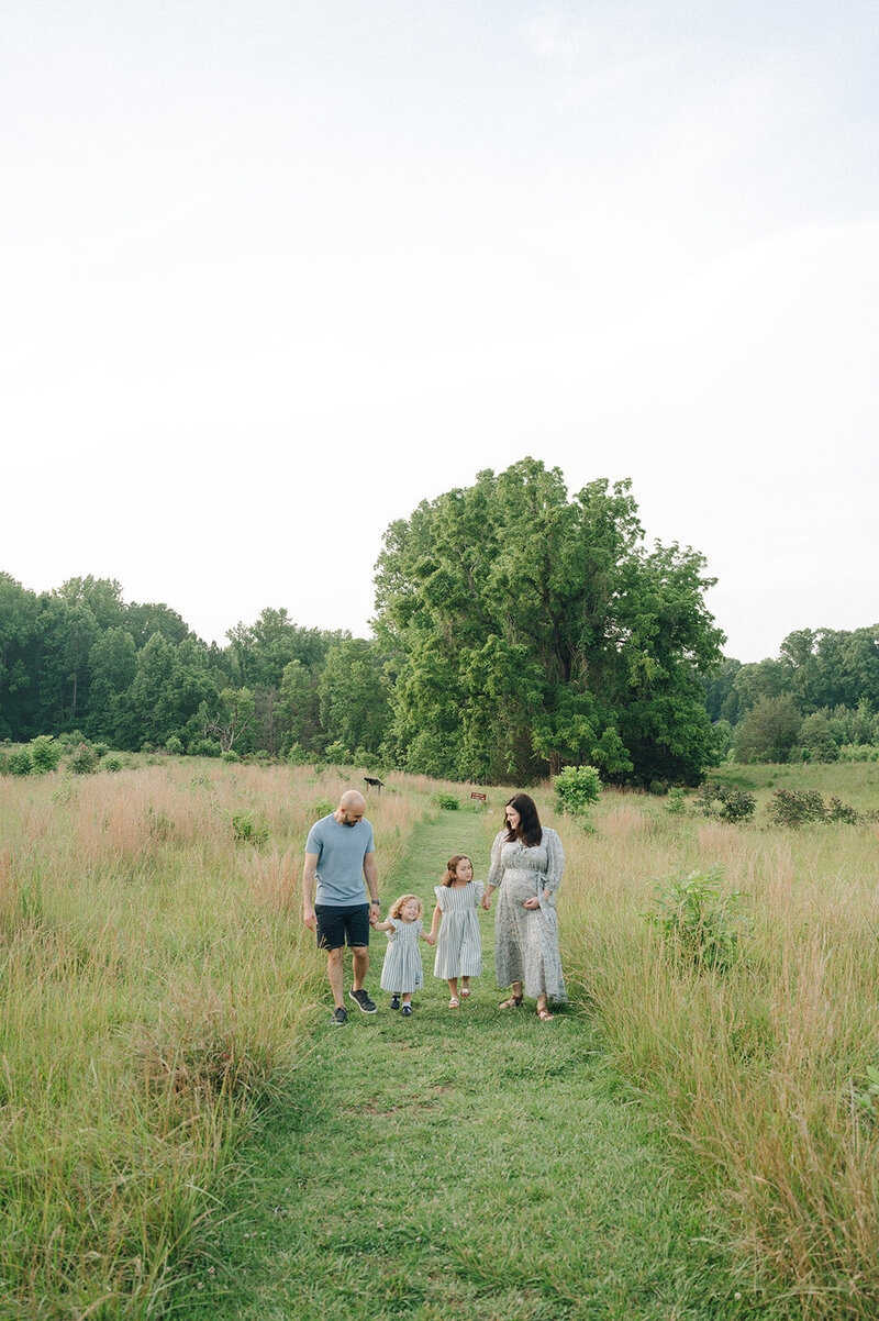 A love-struck couple holding hands, gazing into each other's eyes, and smiling on a sunny day in the midst of a green meadow.