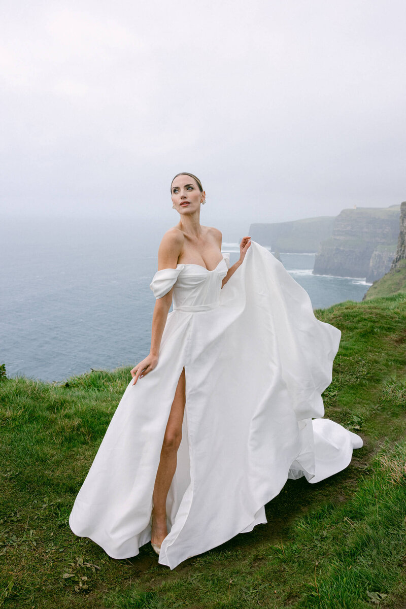 Bride posing for her portrait at the top of the cliffs of Moher with the ocean in the background