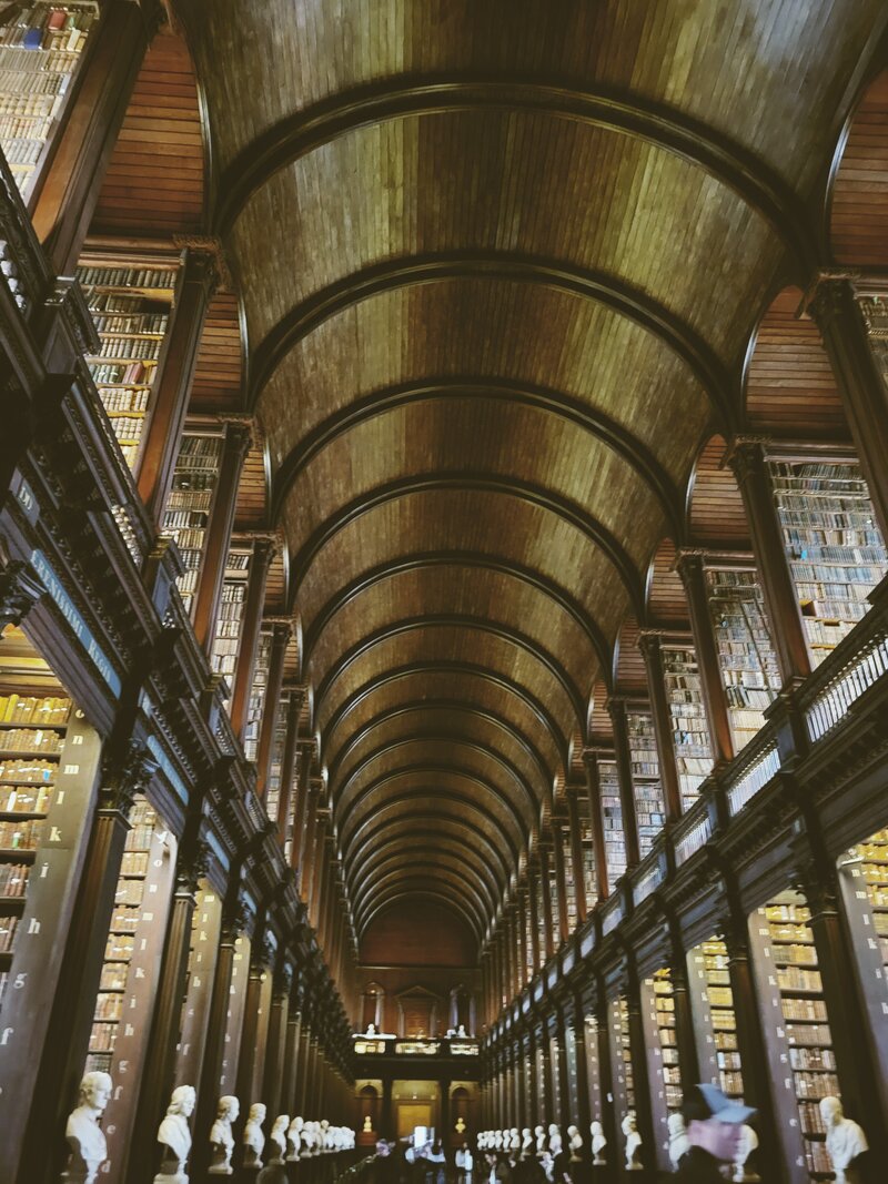 Trinity college library wooden library with over 2 stories high wooden ceiling and bookcases all ornate with busts of famous irishmen in front of each section