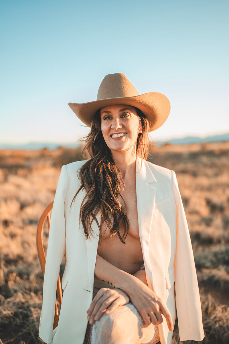 Outdoor brand portrait of Juliet Trnka wearing a brown cowboy hat and light beige blazer, sitting on a chair-part of the Direct Knowing brand photos