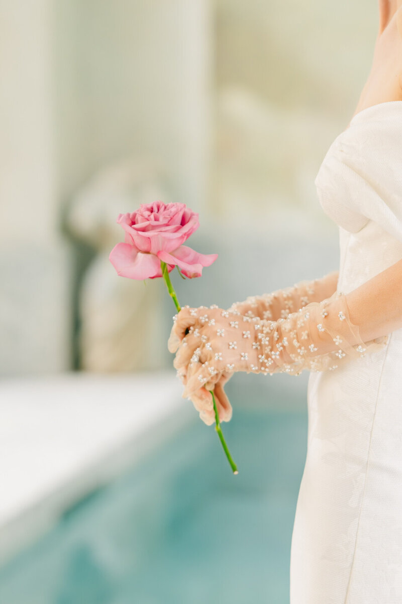bride wearing wedding dress and gloves while holding a pink rose