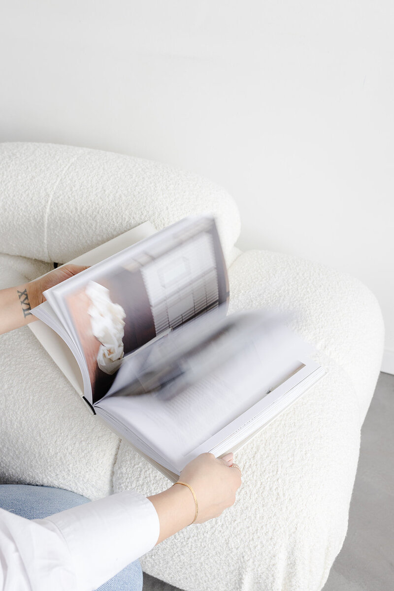 woman's hands flipping through the pages of a book against a plush white couch