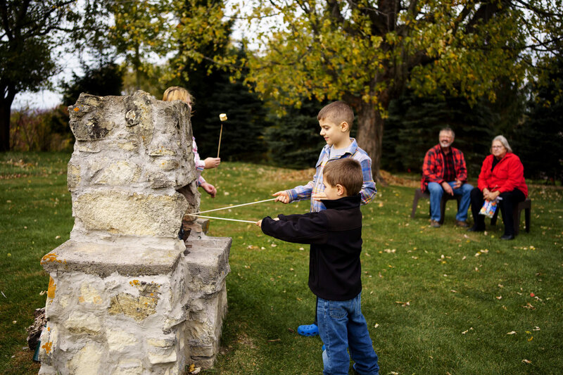 GRANDPARENTS WATCH AS GRANDKIDS ROAST MARSHMELLOWS OUTSIDE OVER FIRE - TREMPEALEAU, WISCONSIN- 50TH WEDDING ANNIVERSARY PHOTOGRAPHY SESSION