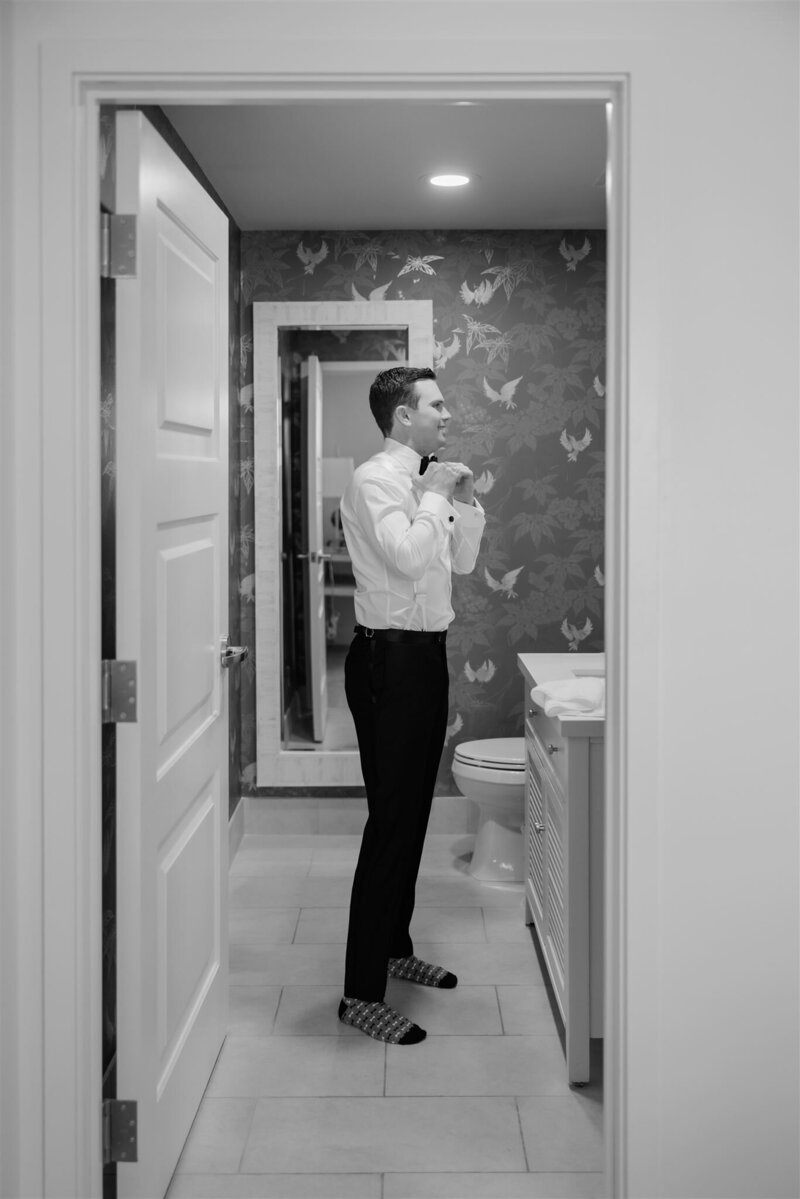 A groom getting ready in the bathroom at the Alfond Inn in a black and white photo. 