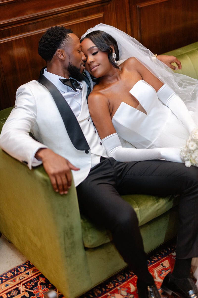 Bride smiles while the groom kisses her cheek in front of a white floral arch.
