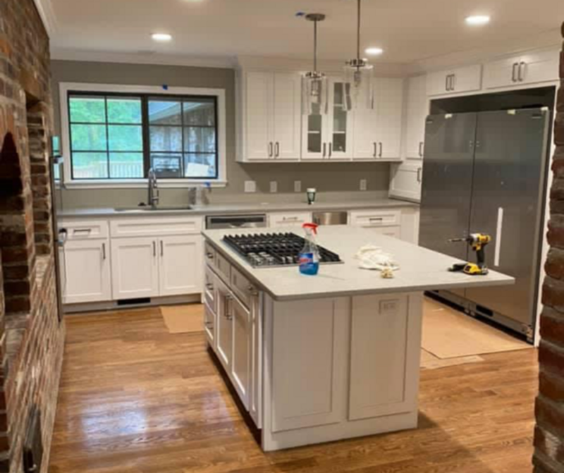 After image of the same kitchen fully remodeled with white cabinets, new floors, and appliances.