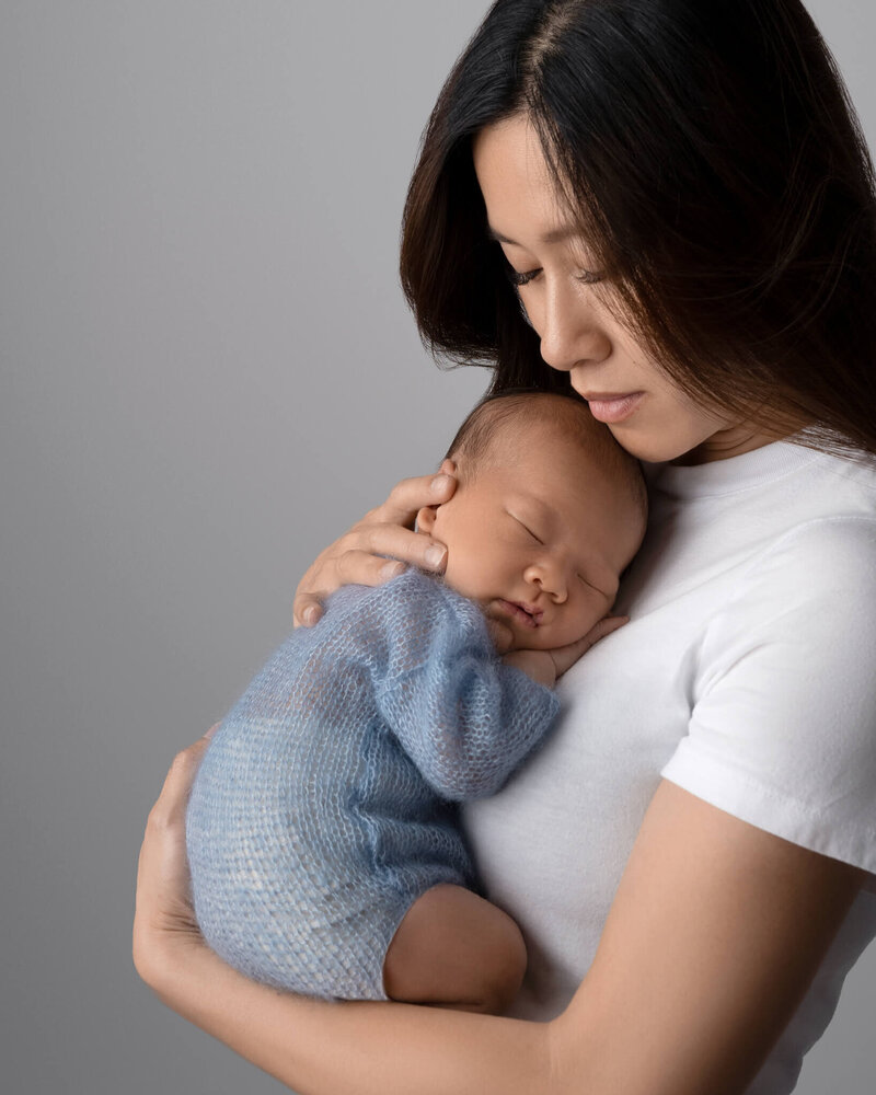 mom wearing white holding her baby boy in a light blue knit outfit