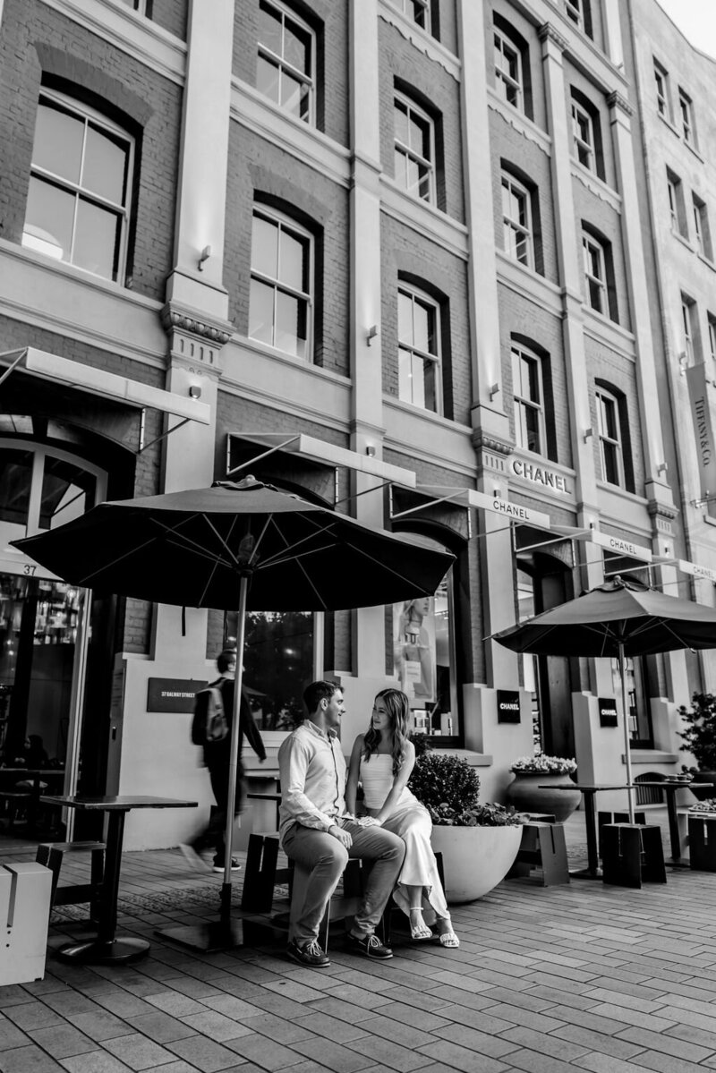 Black and white portrait image of a couple sitting outside a cafe in Auckland City looking at each other captured by Zanthe Vorsatz Photography