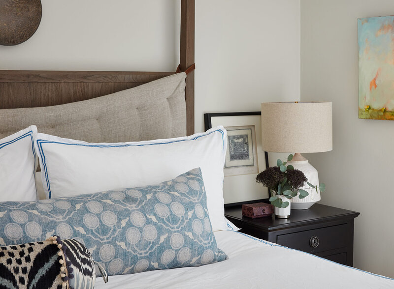 White and blue bed decor with a dark wood nightstand and white lamp