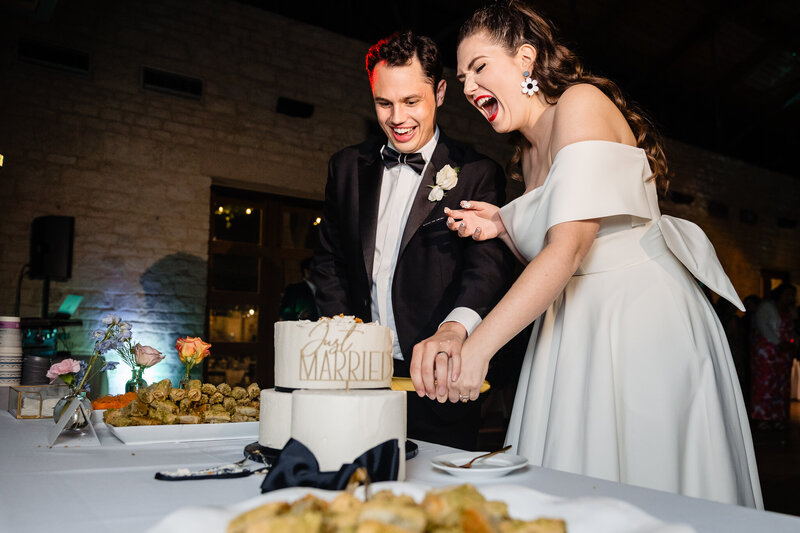 newlywed couple laughs with joy as they cut their wedding cake on their wedding day 