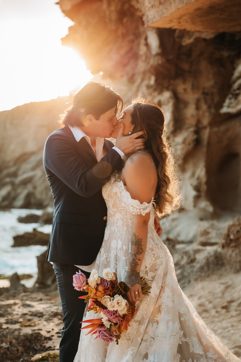 Husband and wife kissing on their wedding day at the beach.