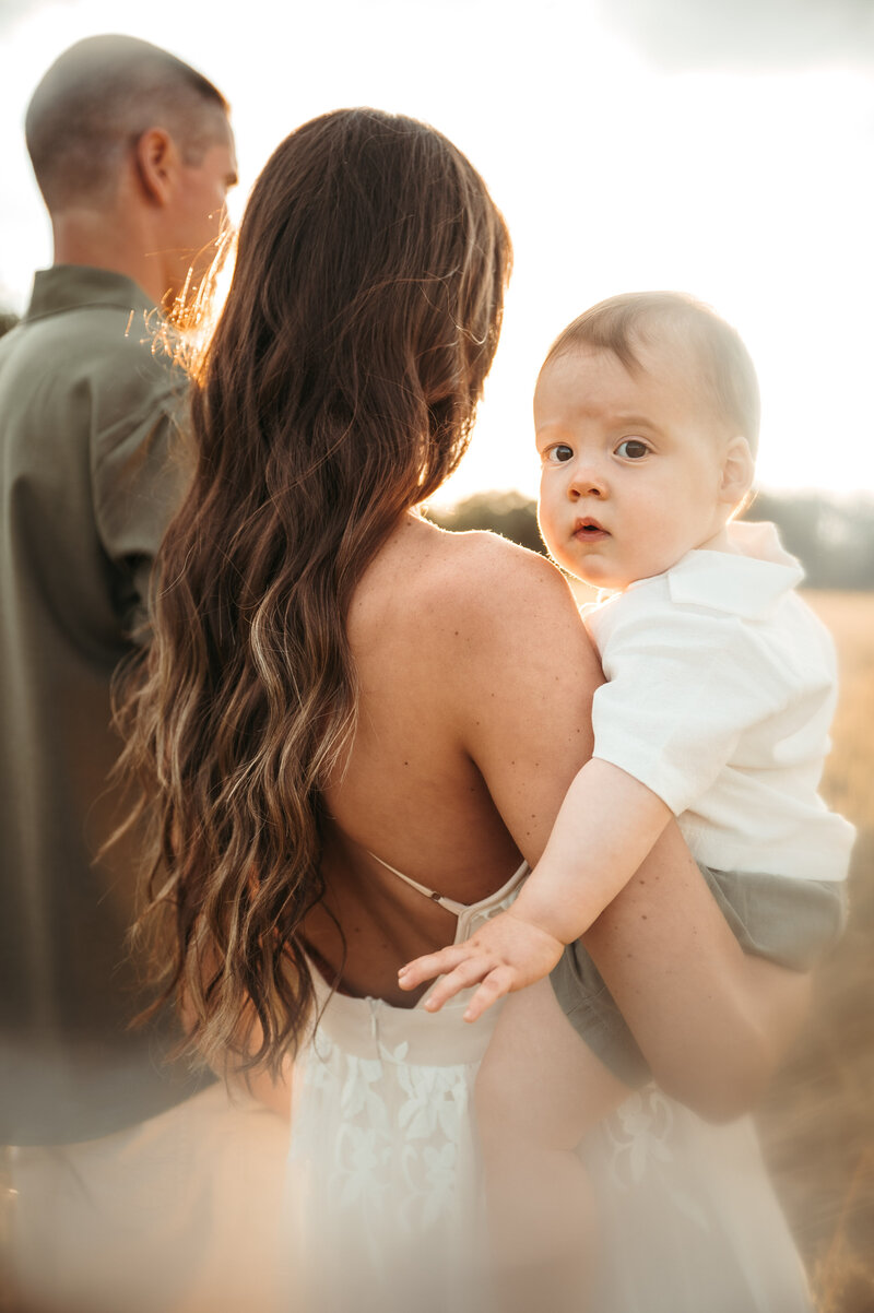 A baby boy in his mother's arms looking over her shoulder. 