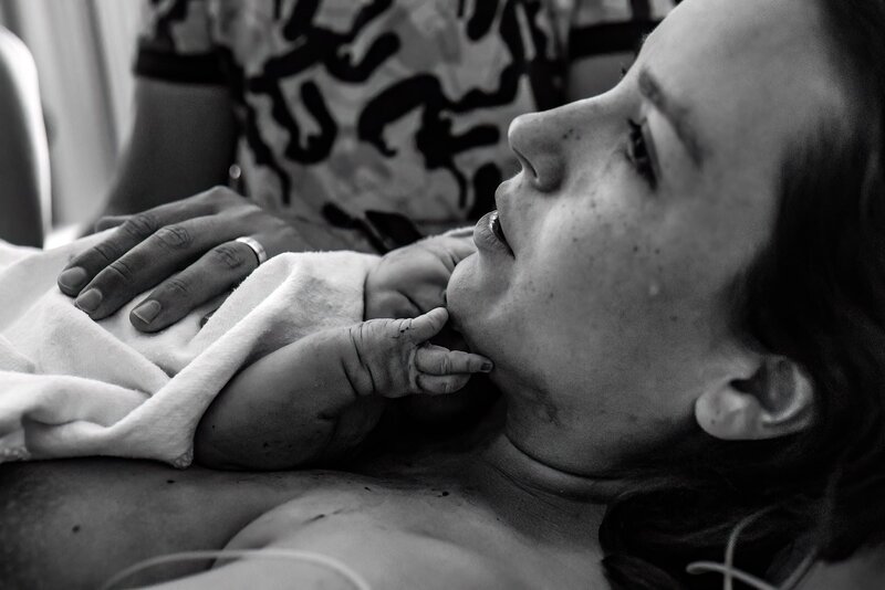 Een emotioneel beeld van een moeder met een traan op haar wang als ze haar baby voor het eerst vast houdt, de baby raakt met haar handje het gezicht van haar moeder aan.
