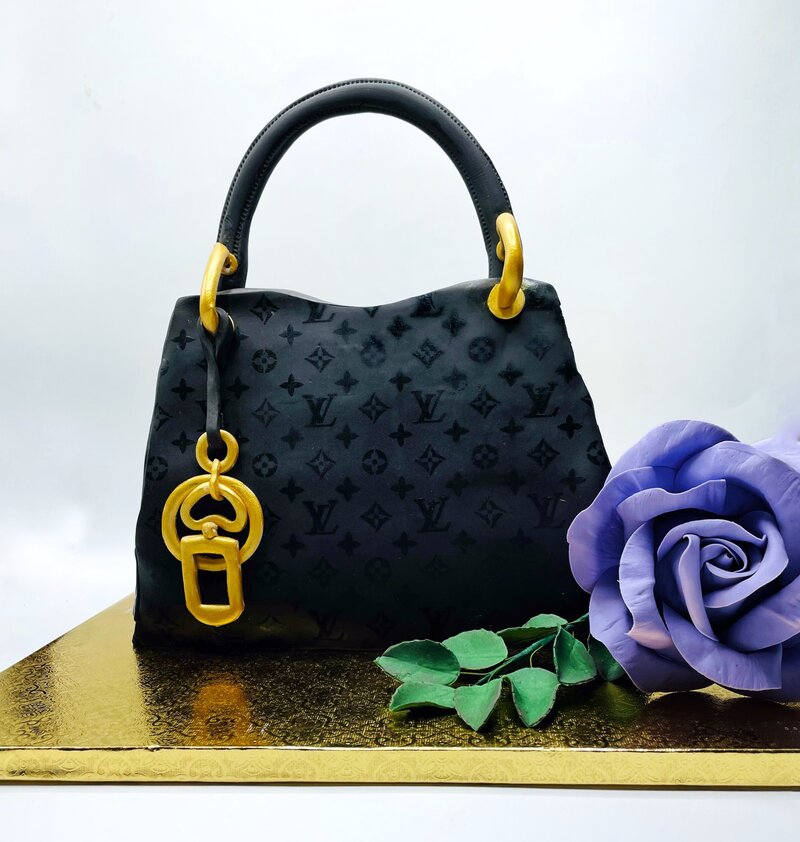 Cake in shape of black Louis Vuitton purse with gold fondant decor and handcrafted purple gumpaste rose