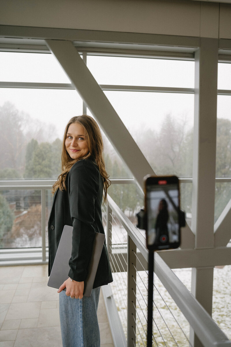 Social media manager with brown hair holding laptop and smiling at camera