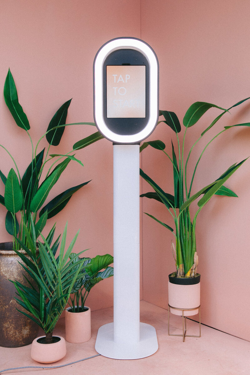 Modern photo booth setup accented with lush green plants, creating a stylish and natural event look