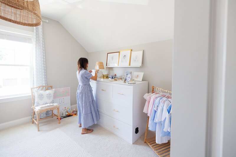 Woman arranging items on a dresser with framed portraits above.