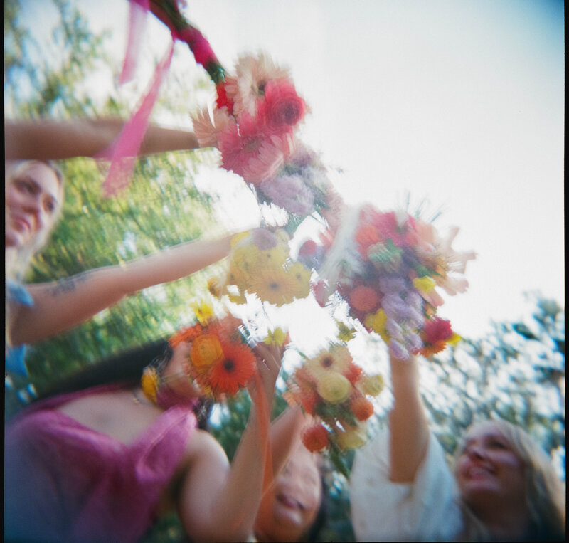 slightly blurred candid photo of bride and bridesmaids raising colorful bouquets at The Wildflower Barn in Driftwood, Texas
