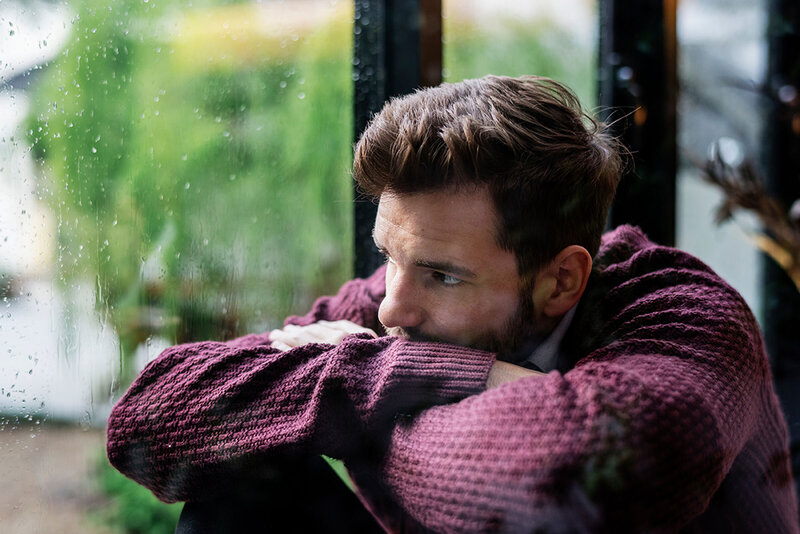 Man sitting in a green velvet chair with his head resting in his hand, conveying stress or contemplation.