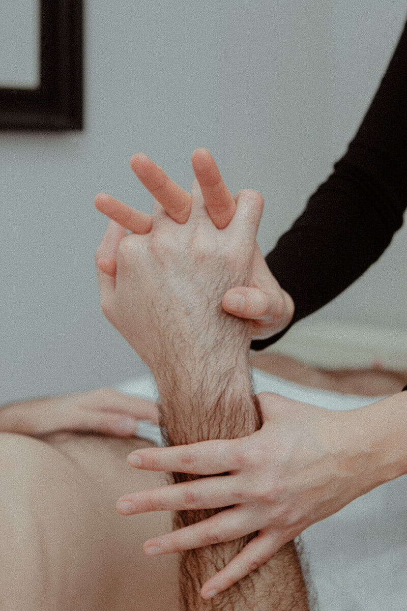 Annie's finger's are interlaced with her male patient's as he lays atop acupuncture table.