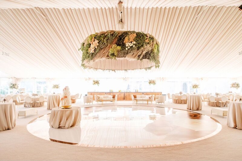 Elegant reception tent with a round dance floor and large floral chandelier.