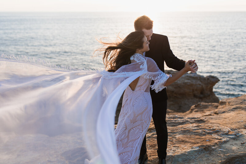 Bride’s dress flowing in the wind as the couple poses on a cliff overlooking the Oregon Coast, captured by an Oregon Coast Elopement and Wedding Photographer.
