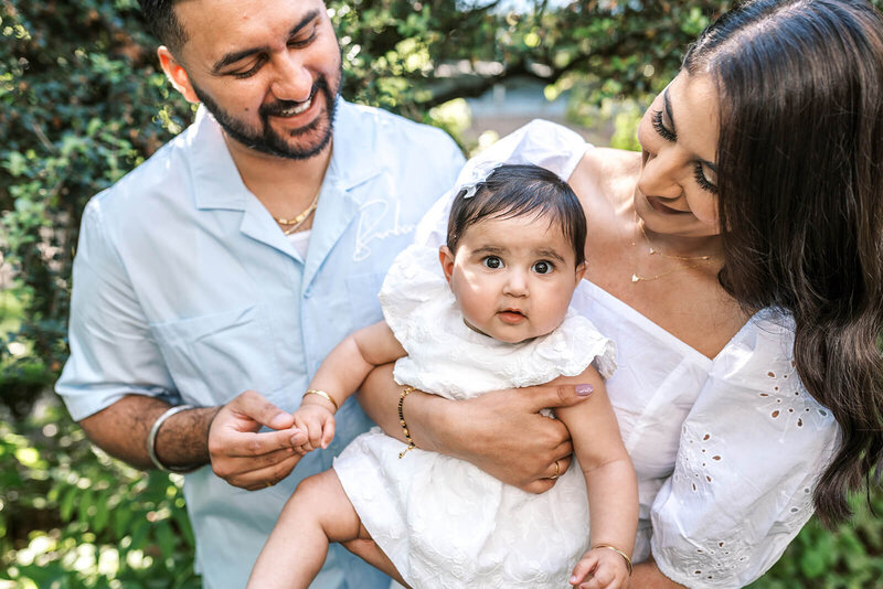 Parents hold their baby and smile at her, representing an example of a family photography portraits session. 