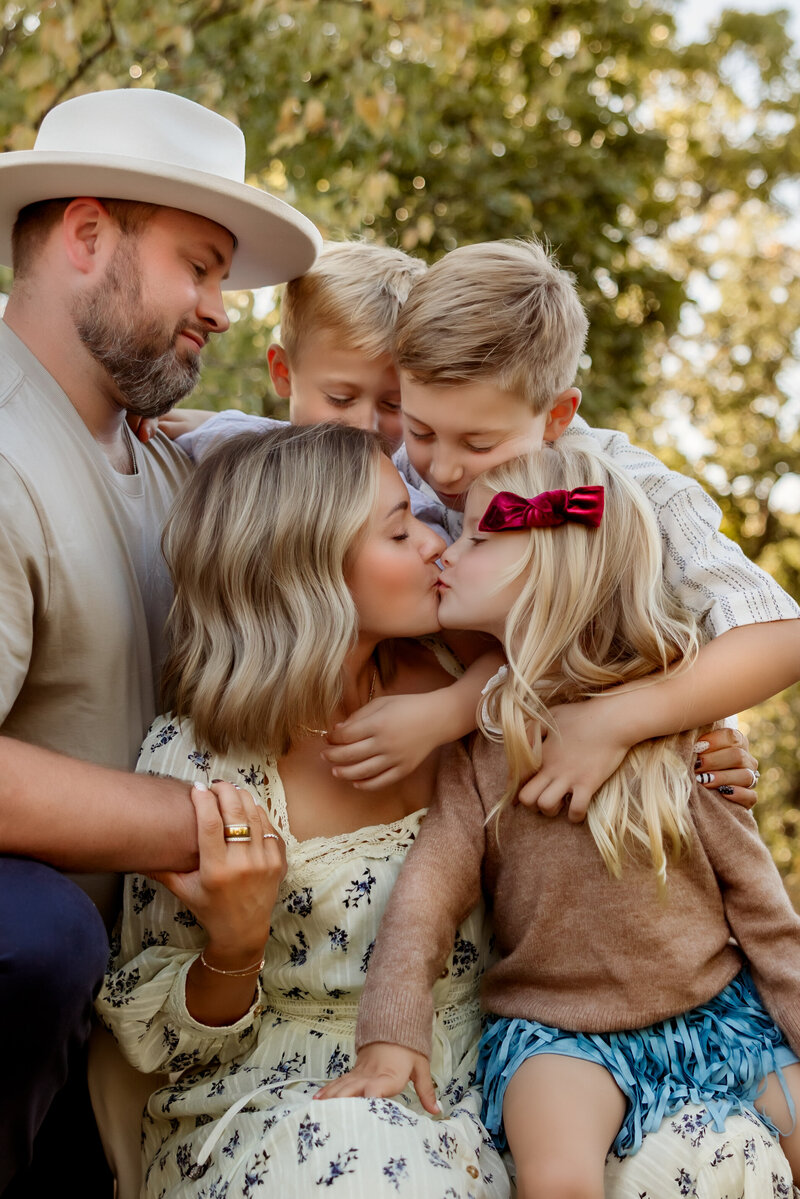 Mom kisses daughter while her two sons and husband hug them during family fall sunset session with Kansas City Lifestyle Photographers.