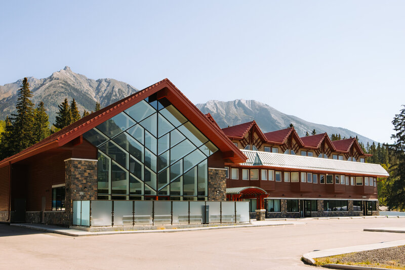 Modern mountain-inspired exterior of The Gem Accommodation in Canmore, Alberta, featuring striking glass architecture, stone accents, and views of the Canadian Rockies.