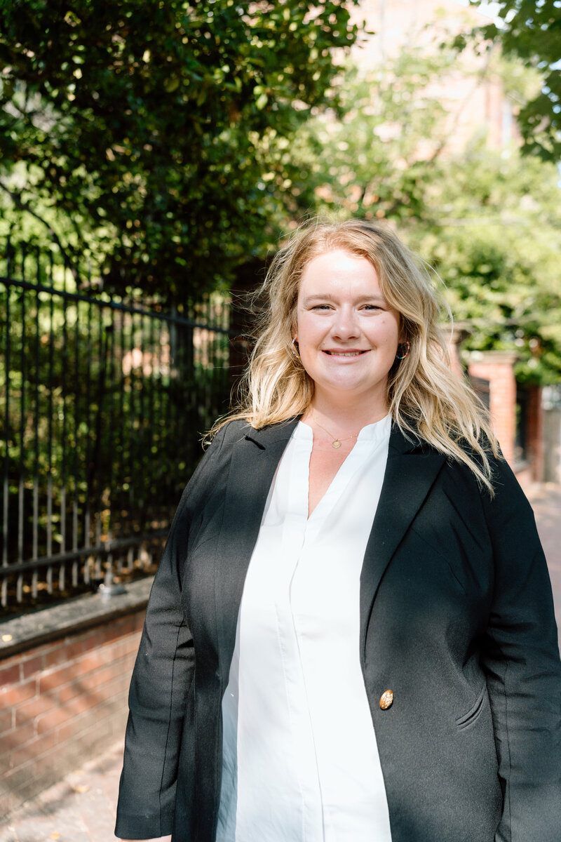 Photo of Emily Lenning - Founder of Blossom Marketing - Walking along a sidewalk in DC with trees and a fence in the background