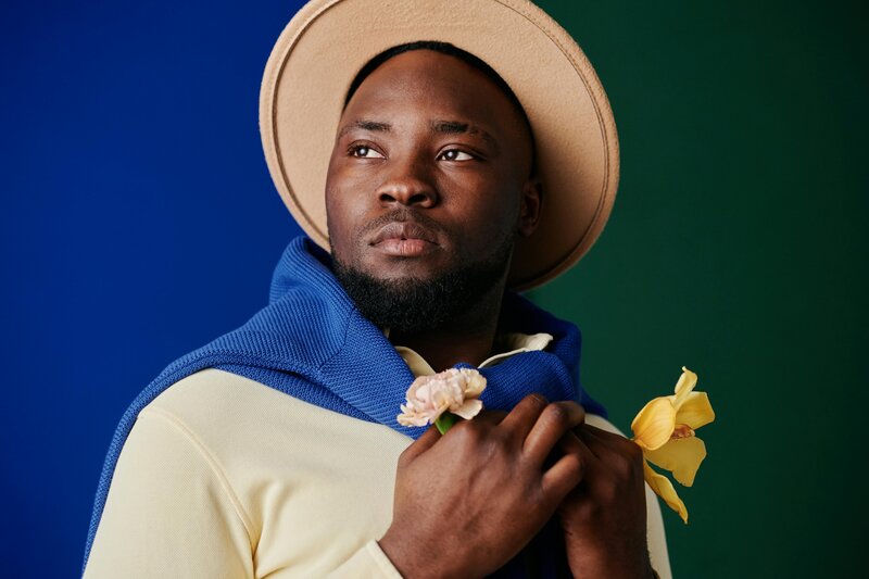 black man on a cobalt blue and dark green brackdrop with flowers in his hands