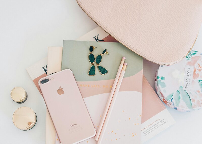 Flat lay with pink iPhone, green earrings, pencils, purse, and floral pouch styled for leadership coaching workspace