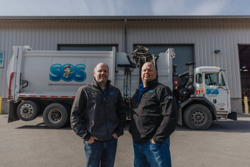 two men standing in front of garbage truck