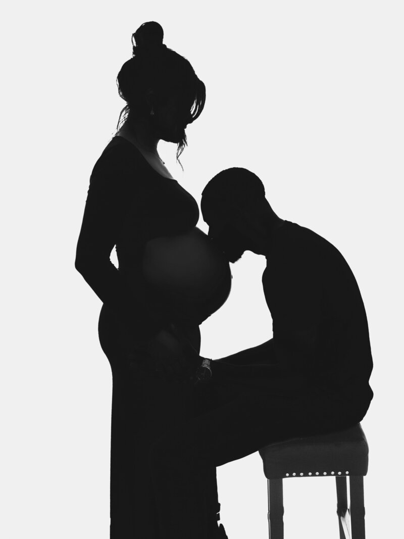 a silhouette of a man kissing his pregnant wife's belly