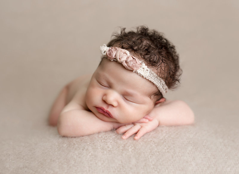 newborn girl posed on tan blanket