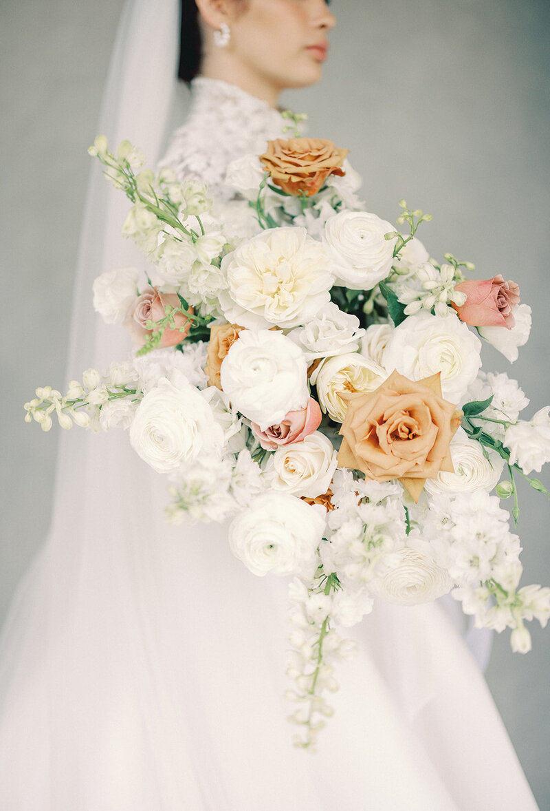 Close-up of a bride holding a large bouquet of white, orange and green florals