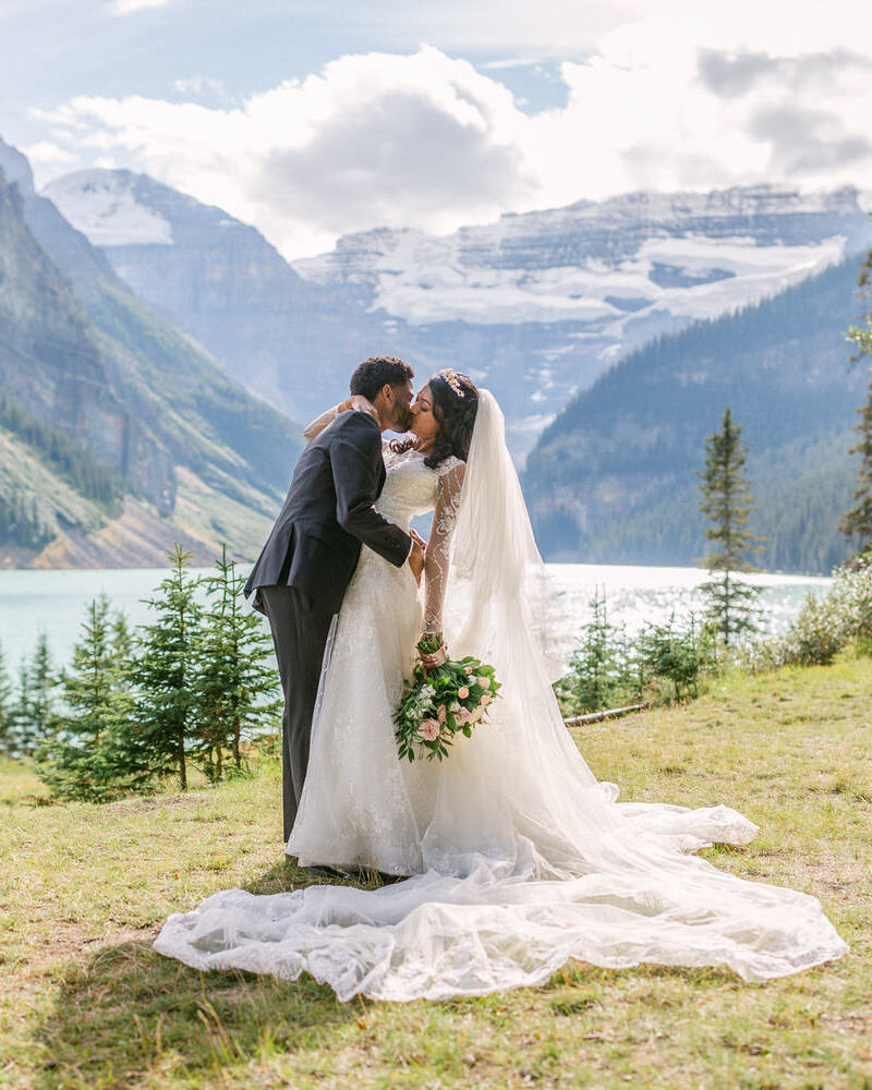 A romantic moment as the groom bends the bride back for a kiss at Chateau Lake Louise, with turquoise waters and Victoria Glacier as the backdrop.