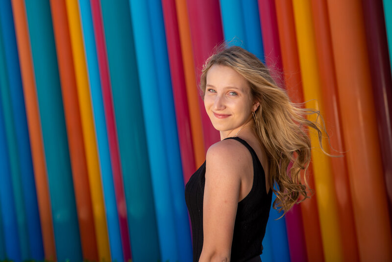 Teenage girl smiles for senior portraits in front of brightly colored wall