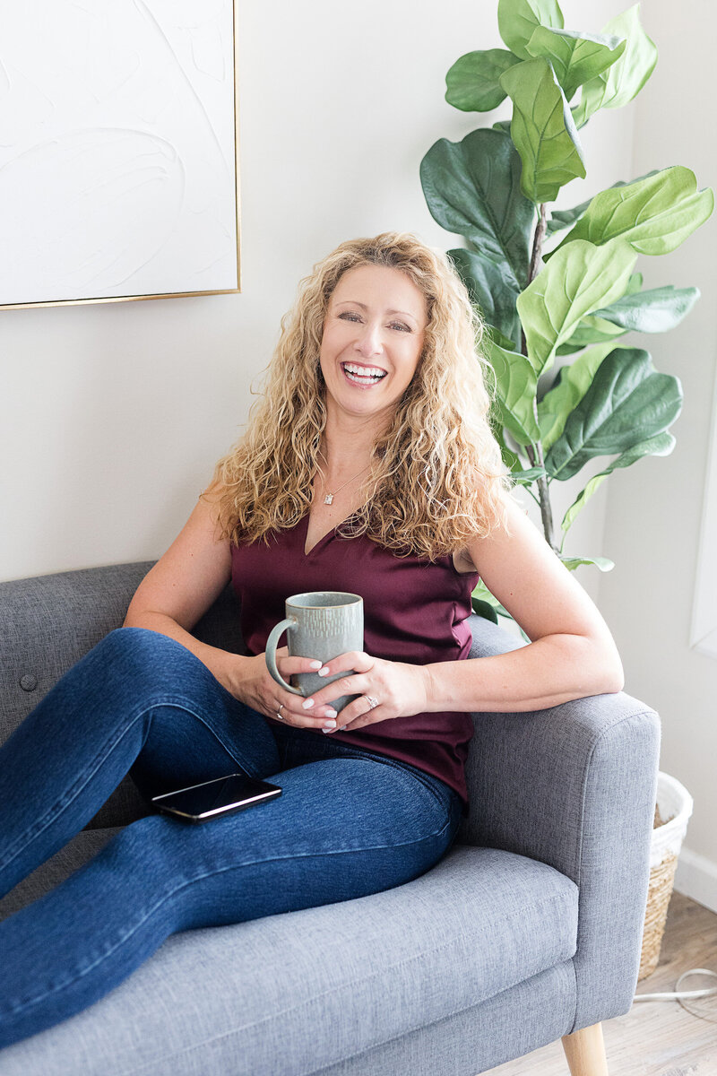 Kathleen sitting on a couch with a cup of coffee in hand, smiling