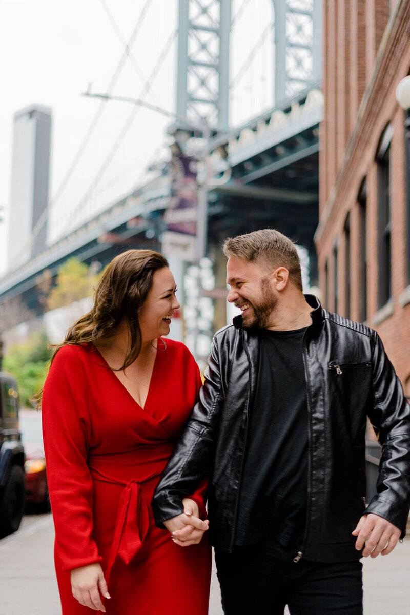 couple holding hands and looking at each other as they walk down a sidewalk laughing