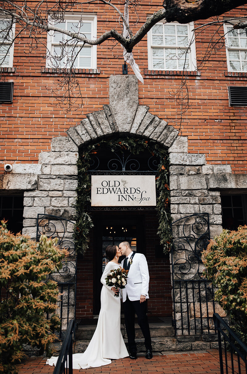 Bride and groom share a romantic kiss in front of Old Edwards Inn in Highlands, NC - captured during a cozy and elegant mountain wedding.