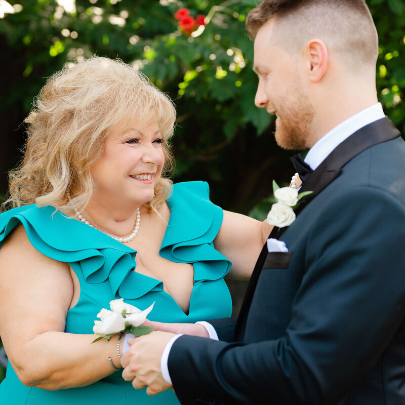 a mother of the groom in a green dress smiles happily at the groom.  Taken outdoors by Ottawa wedding photographer JEMMAN Photography