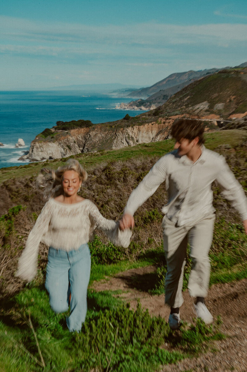 Big Sur Couples Photographer- couple running together with Big Sur coastline in the background