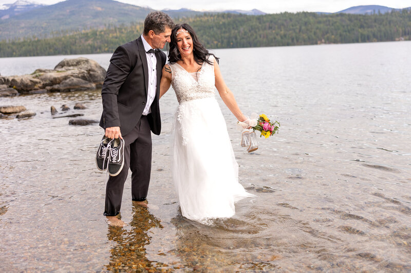 Bride and Groom walking hand in hand barefoot in Priest Lake smiling at each other