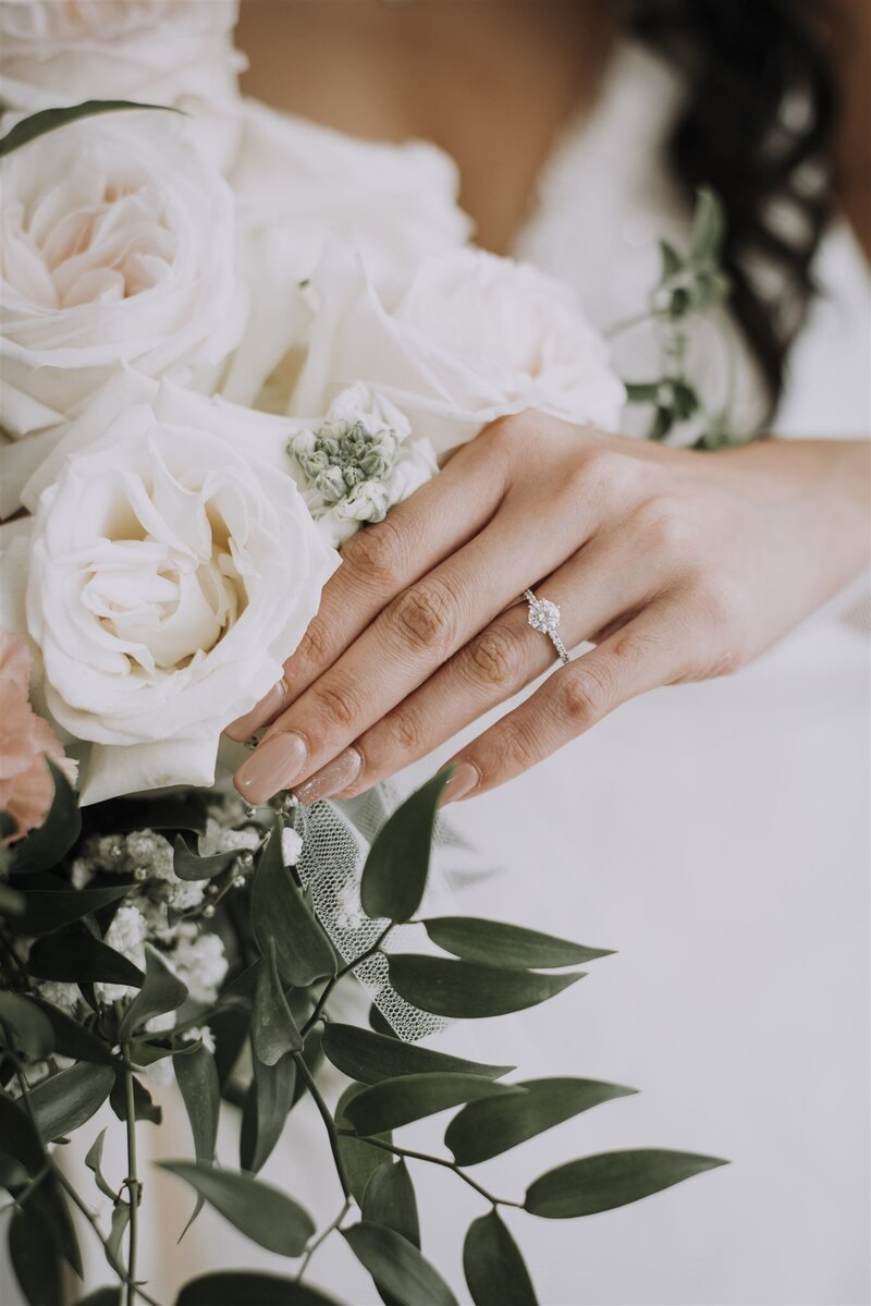 Romantic close-up of bride and groom’s hands with wedding rings and white floral bouquet.