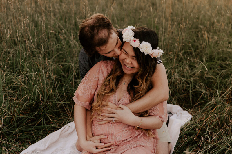 Husband kissing pregnant wife while sitting in grass