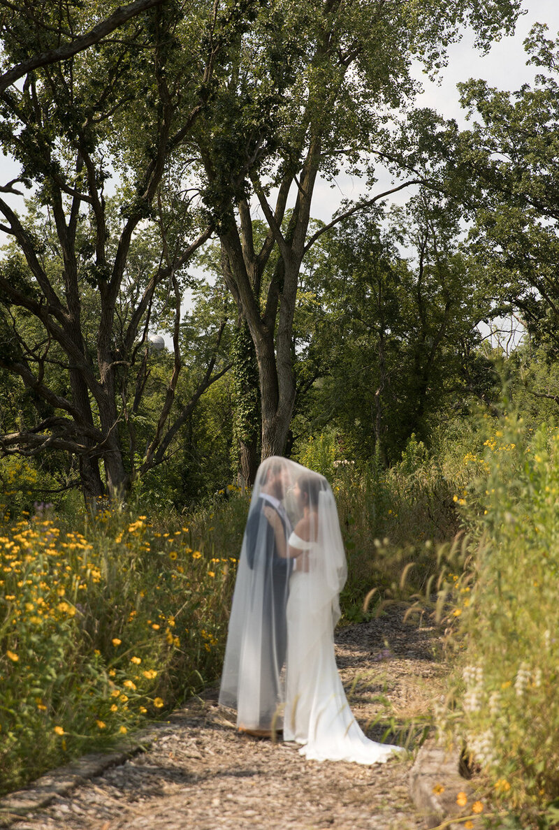Bride and groom walking hand in hand on a wildflower-lined path during an international wedding ceremony.