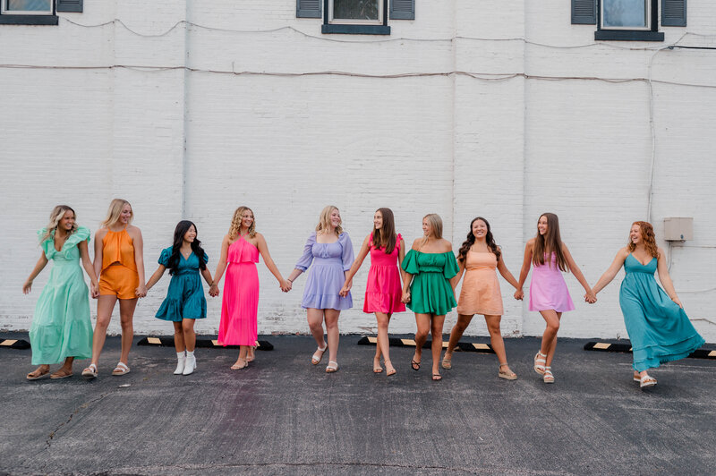 Rachel B Photography's Senior Rep Team of 14 seniors walk hand in hand in an open field  while smiling at one another.